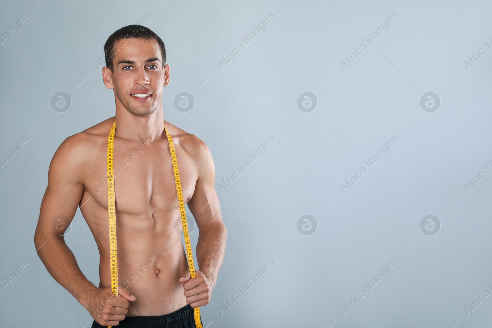 Handsome shirtless man with slim body and measuring tape on grey background. Space for text Photo of Handsome shirtless man with slim body and measuring tape on grey background. Space for text