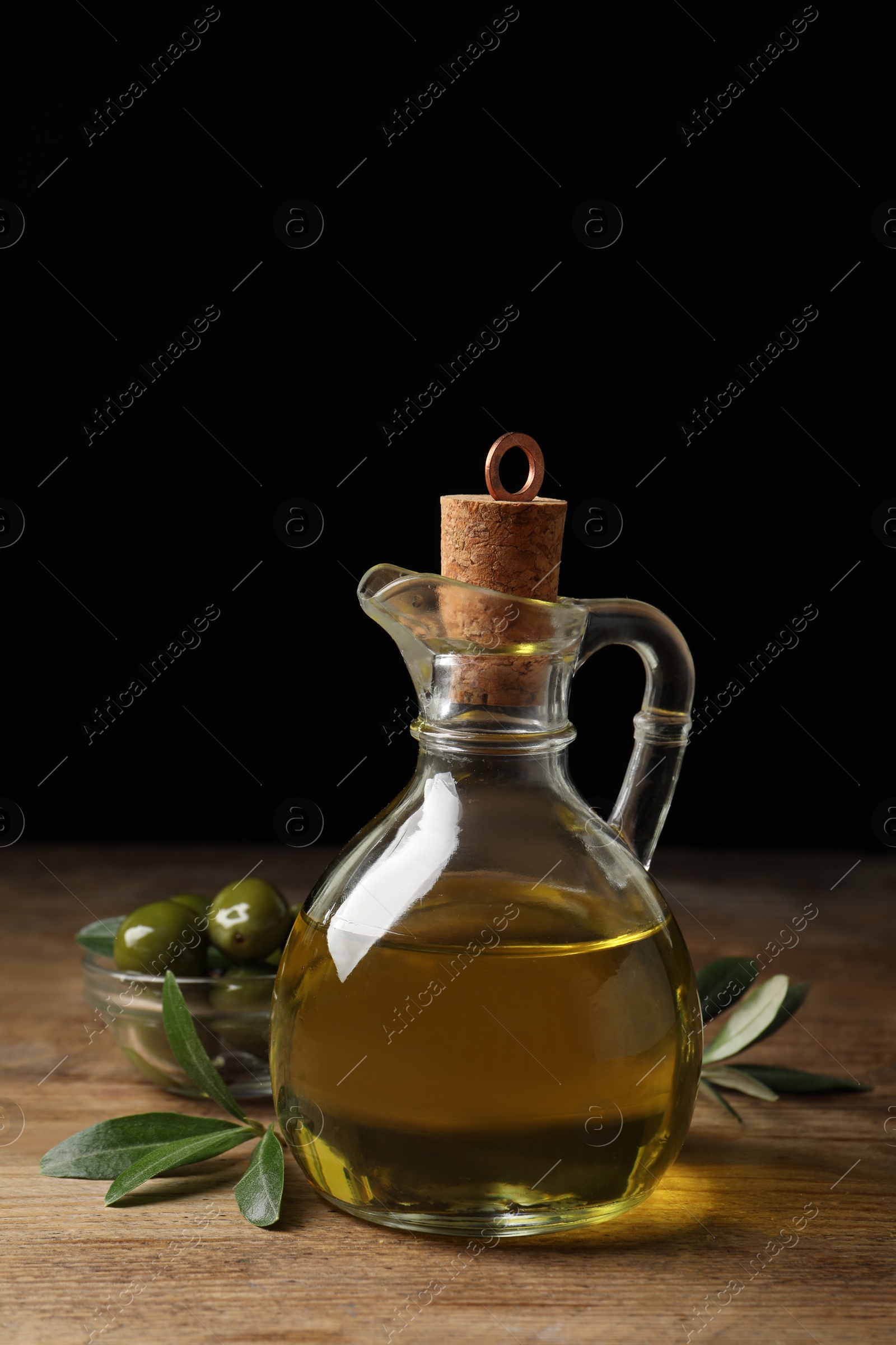 Glass jug of oil, ripe olives and green leaves on wooden table Photo of Glass jug of oil, ripe olives and green leaves on wooden table