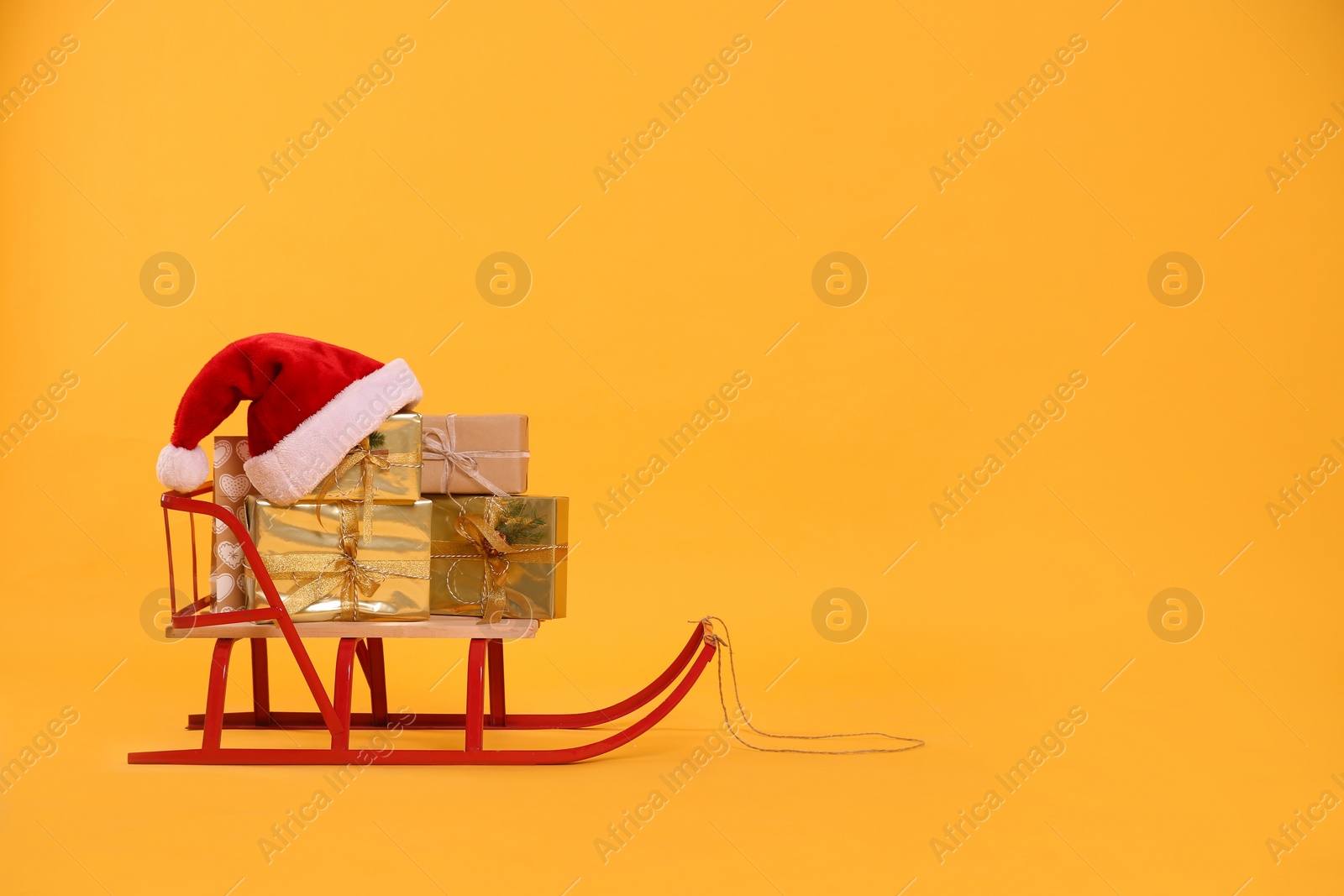 Sleigh with gift boxes and Santa hat on yellow background. Space for text Photo of Sleigh with gift boxes and Santa hat on yellow background. Space for text