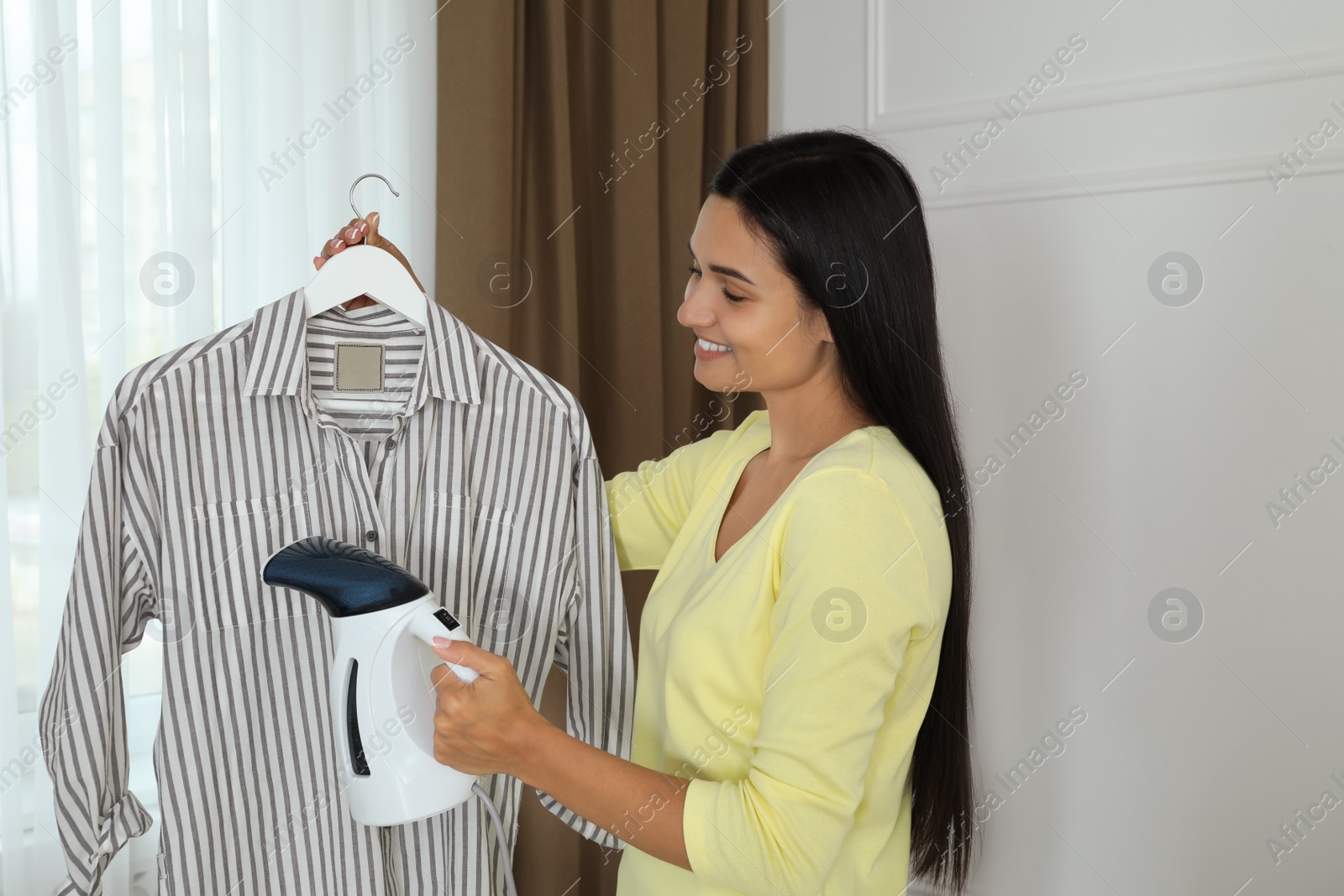 Woman steaming shirt on hanger at home Photo of Woman steaming shirt on hanger at home