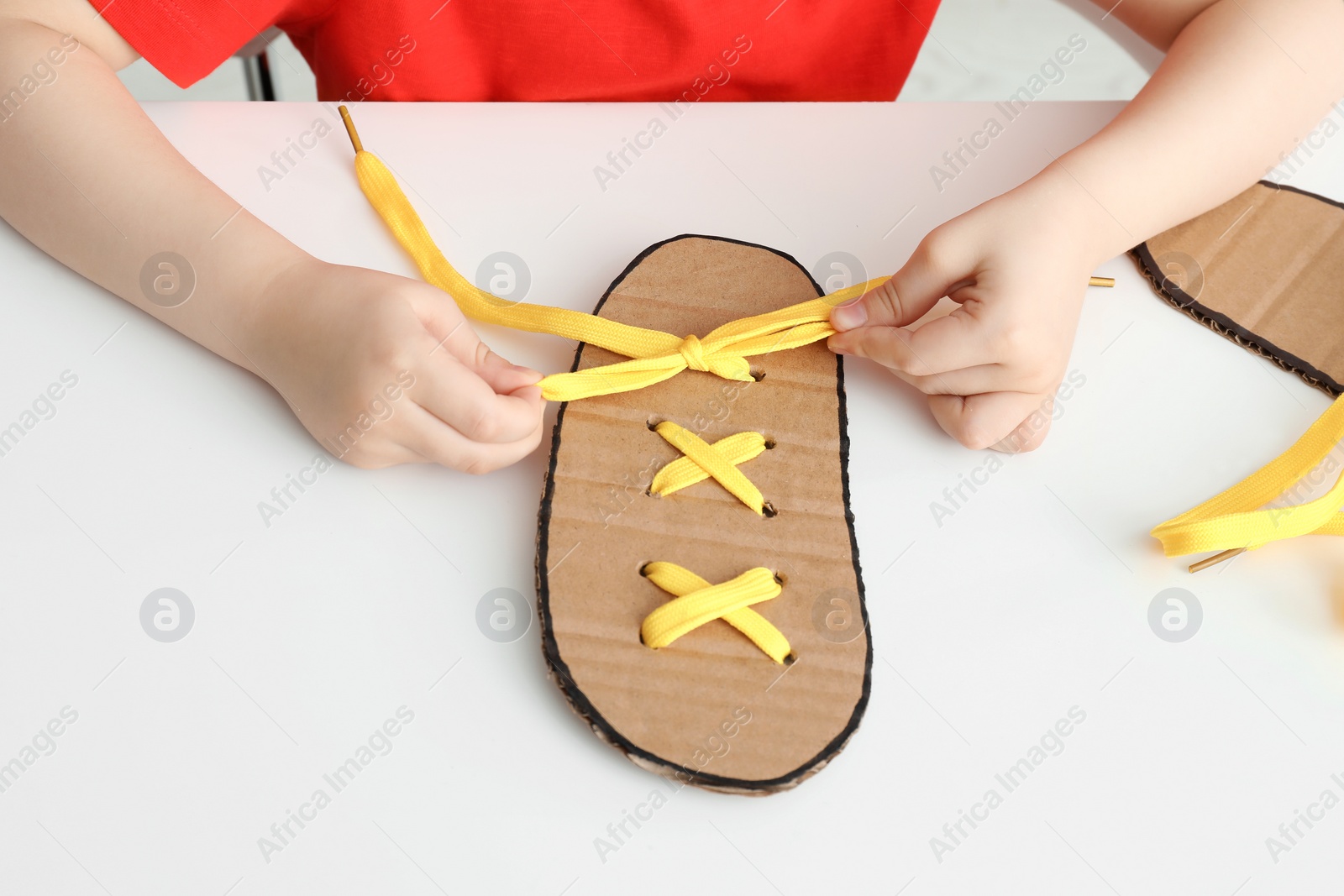 Little boy tying shoe lace using training cardboard template at white table, closeup Photo of Little boy tying shoe lace using training cardboard template at white table, closeup