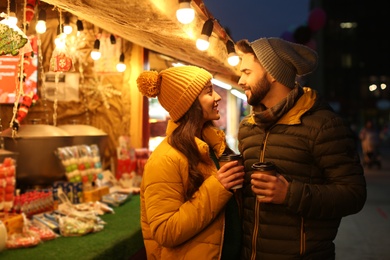 Lovely couple with cups of hot drinks spending time together at Christmas fair Photo of Lovely couple with cups of hot drinks spending time together at Christmas fair