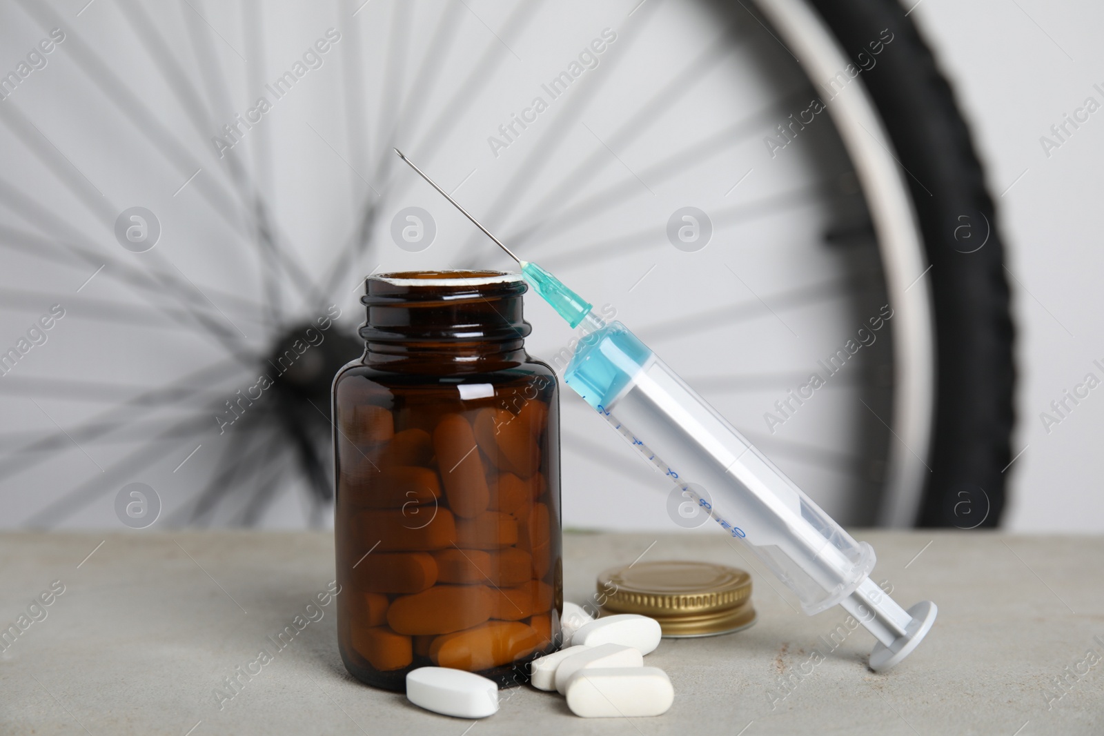 Pills and syringe on light grey table near bike wheel. Using doping in cycling sport concept Photo of Pills and syringe on light grey table near bike wheel. Using doping in cycling sport concept