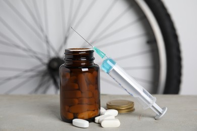 Pills and syringe on light grey table near bike wheel. Using doping in cycling sport concept Photo of Pills and syringe on light grey table near bike wheel. Using doping in cycling sport concept