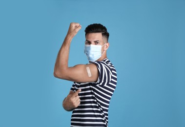 Vaccinated man with protective mask showing medical plaster on his arm against light blue background Photo of Vaccinated man with protective mask showing medical plaster on his arm against light blue background