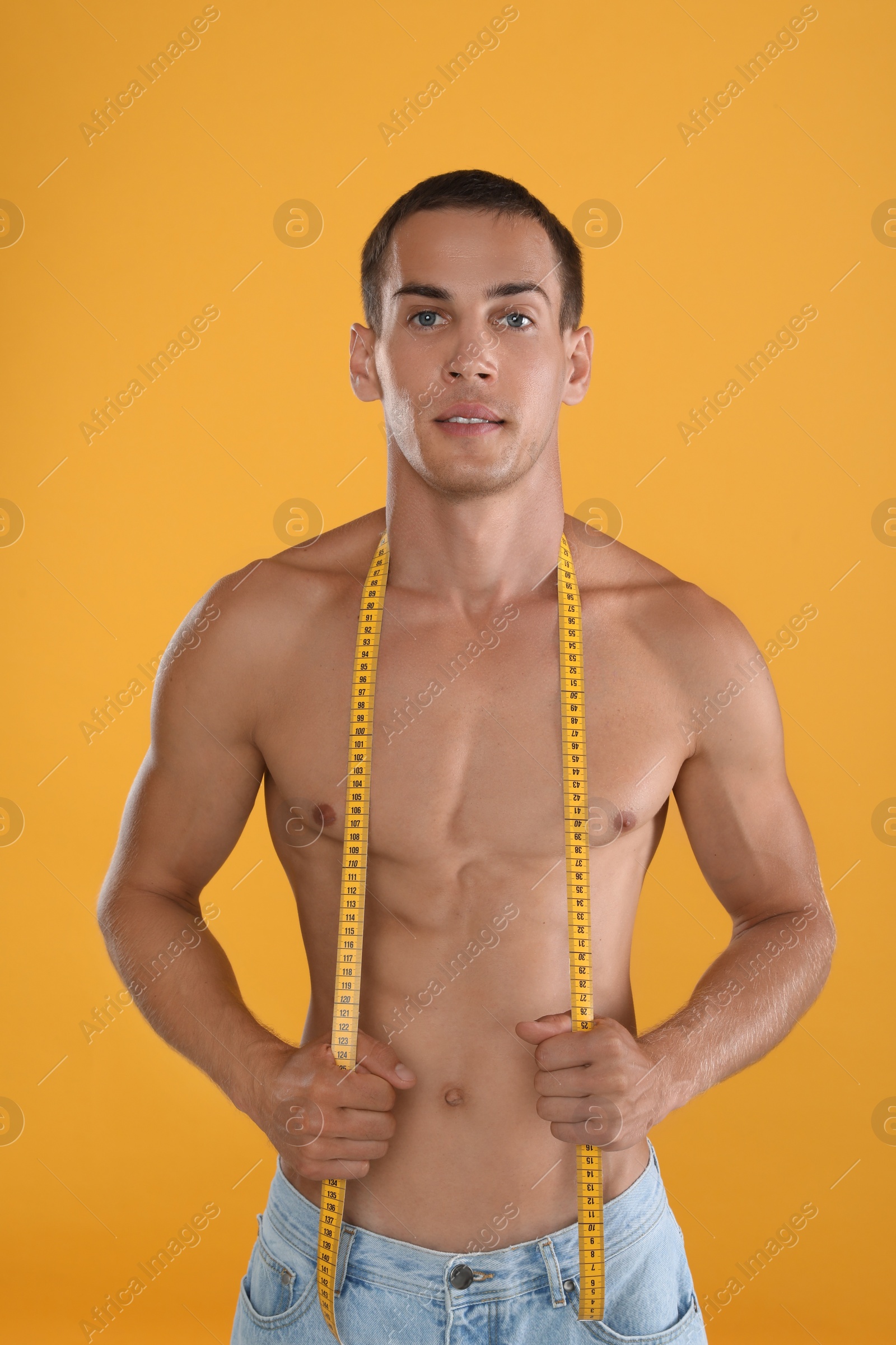 Handsome shirtless man with slim body and measuring tape on yellow background Photo of Handsome shirtless man with slim body and measuring tape on yellow background