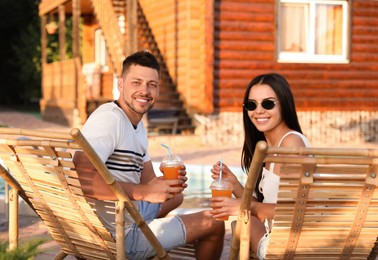 Happy couple with cups of refreshing drink resting in deck chairs outdoors Image of Happy couple with cups of refreshing drink resting in deck chairs outdoors