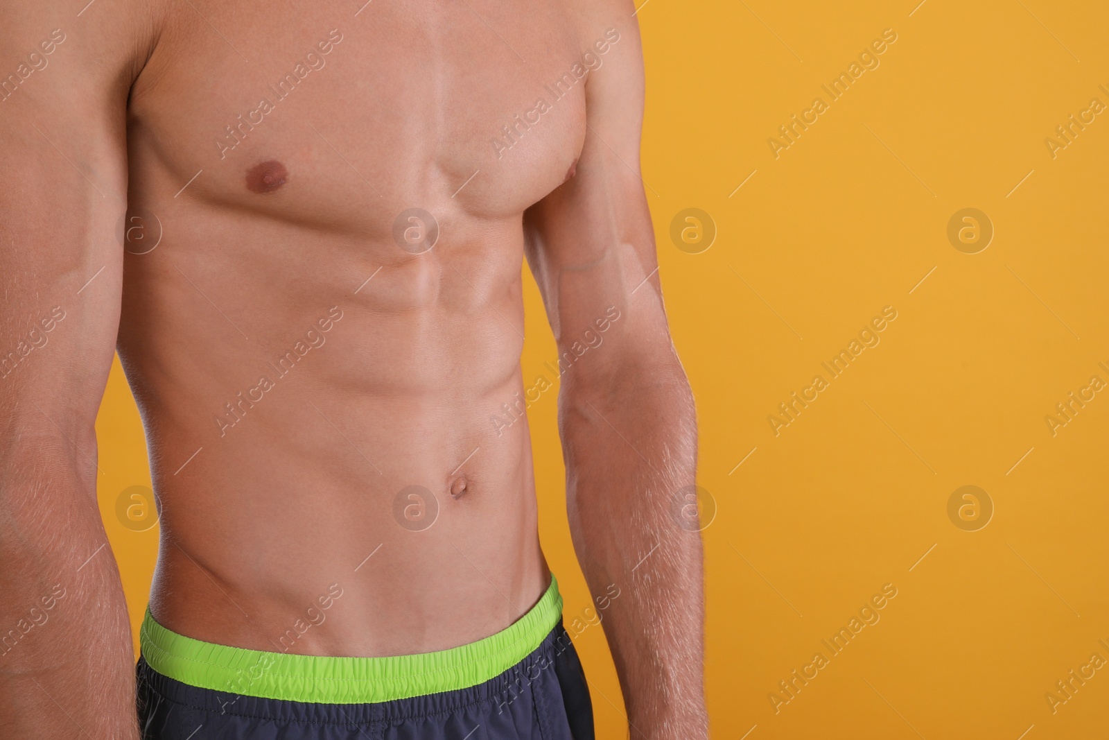 Shirtless man with slim body on yellow background, closeup. Space for text Photo of Shirtless man with slim body on yellow background, closeup. Space for text
