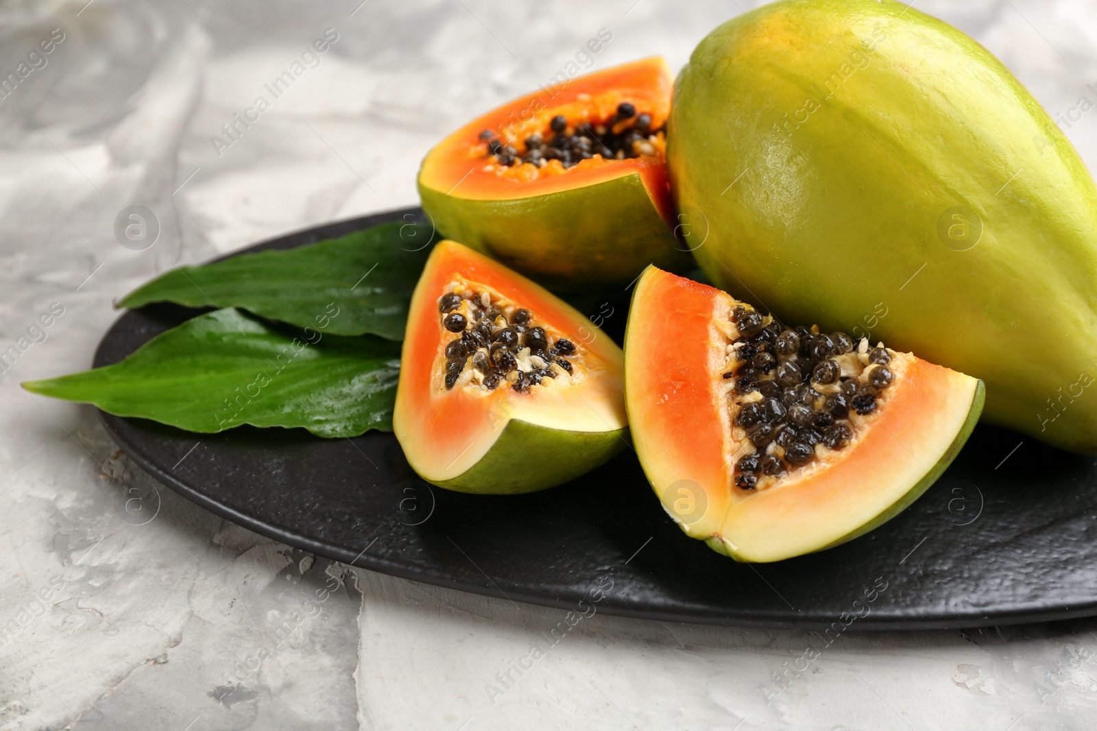 Fresh ripe papaya fruits with green leaves on grey table Photo of Fresh ripe papaya fruits with green leaves on grey table
