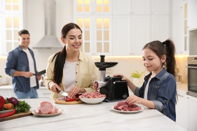 Happy family making dinner together in kitchen, little girl using modern meat grinder while her mother cutting onion Photo of Happy family making dinner together in kitchen, little girl using modern meat grinder while her mother cutting onion