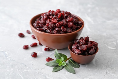 Tasty dried cranberries and leaves in bowls on grey table Photo of Tasty dried cranberries and leaves in bowls on grey table