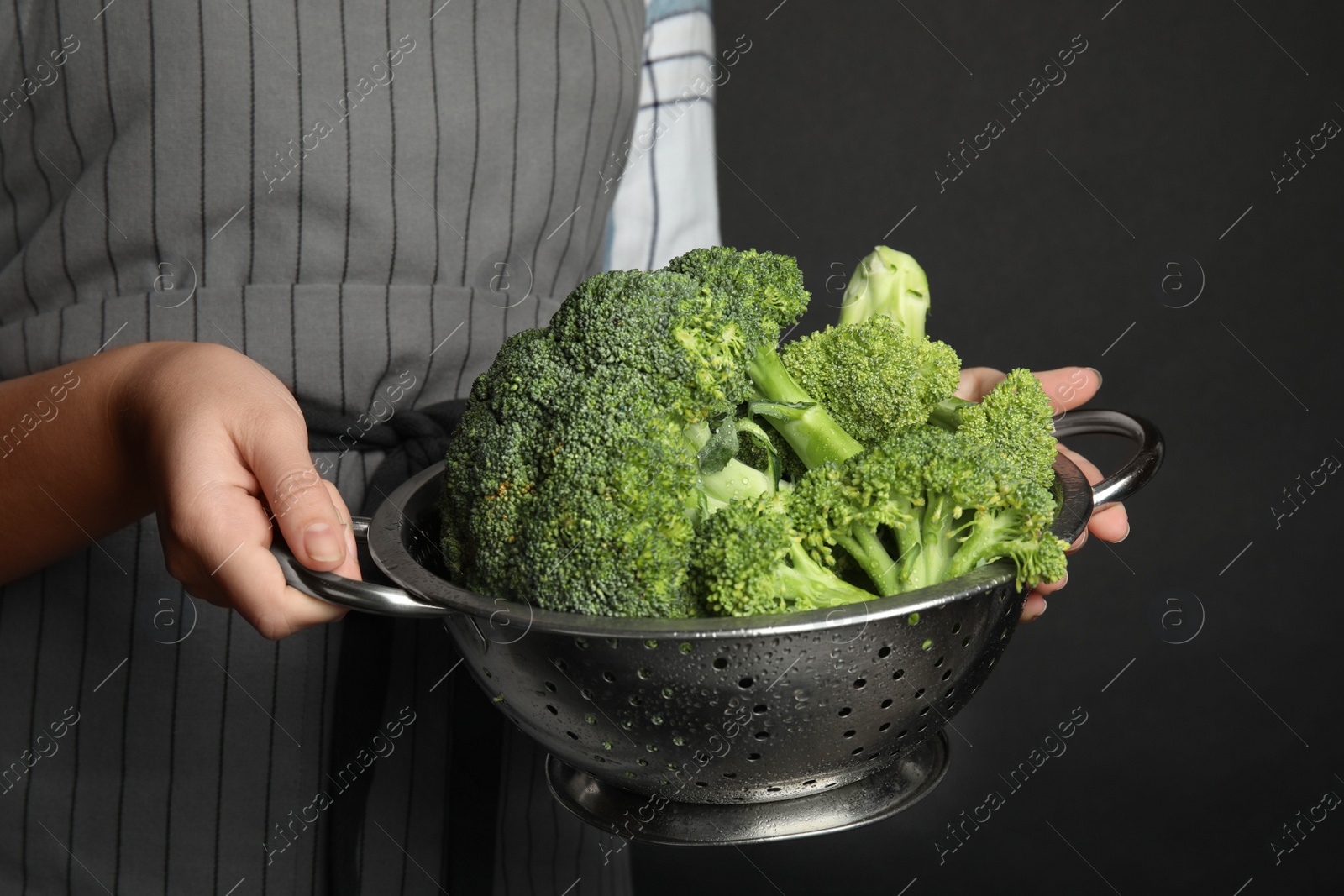 Woman holding colander with fresh green broccoli on black background, closeup Photo of Woman holding colander with fresh green broccoli on black background, closeup