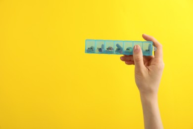 Woman holding plastic box with different pills on yellow background, closeup. Space for text Photo of Woman holding plastic box with different pills on yellow background, closeup. Space for text