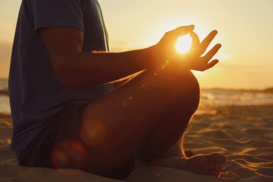 Man meditating on sandy beach at sunset, closeup Photo of Man meditating on sandy beach at sunset, closeup