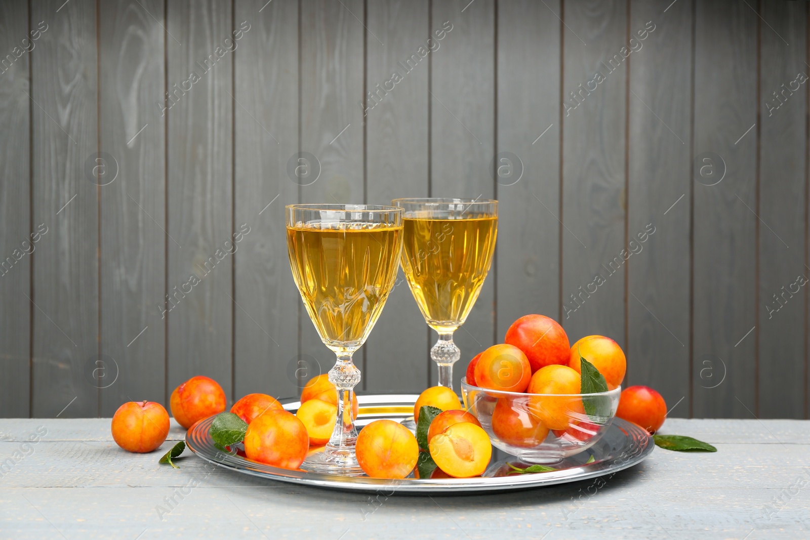 Delicious plum liquor and ripe fruits on table against grey background. Homemade strong alcoholic beverage Photo of Delicious plum liquor and ripe fruits on table against grey background. Homemade strong alcoholic beverage