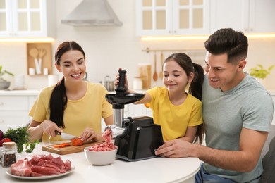 Happy family making dinner together in kitchen, father and daughter using modern meat grinder while mother cutting carrot Photo of Happy family making dinner together in kitchen, father and daughter using modern meat grinder while mother cutting carrot