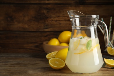 Photo of Cool freshly made lemonade in glass pitcher on wooden table. Space for text