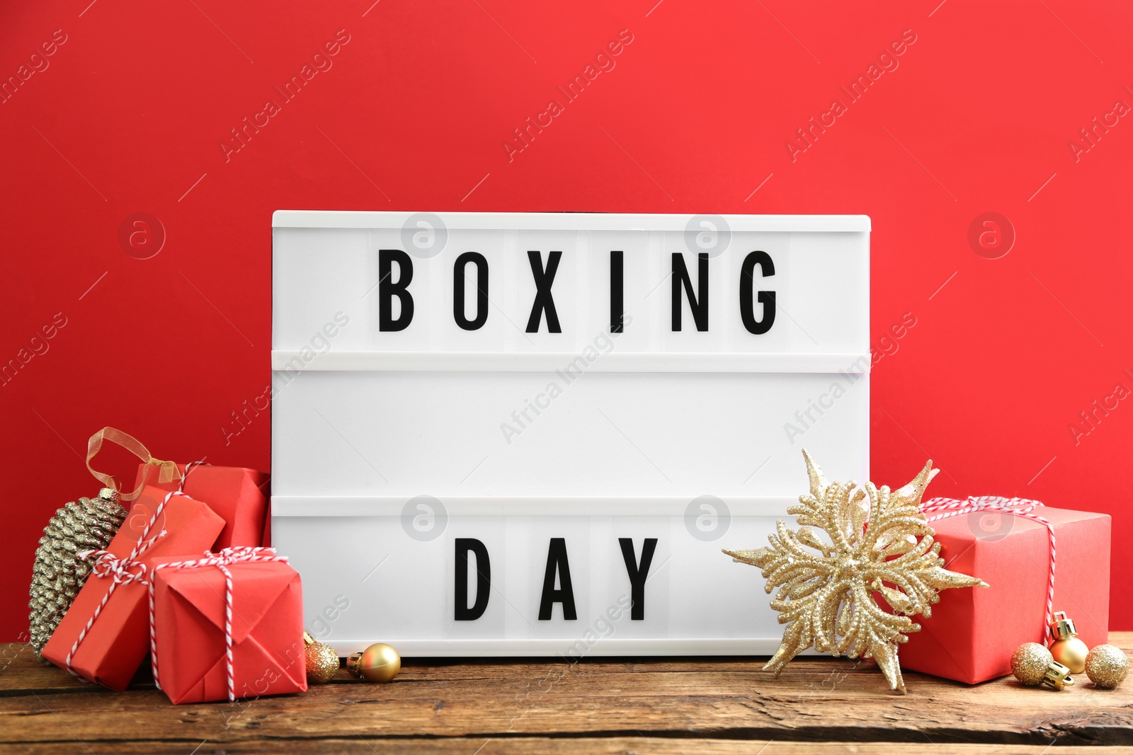 Composition with Boxing Day sign and Christmas gifts on wooden table against red background Photo of Composition with Boxing Day sign and Christmas gifts on wooden table against red background