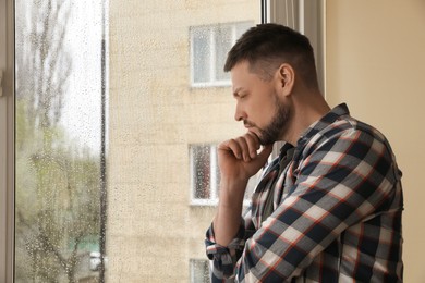 Depressed man near window at home. Space for text Photo of Depressed man near window at home. Space for text
