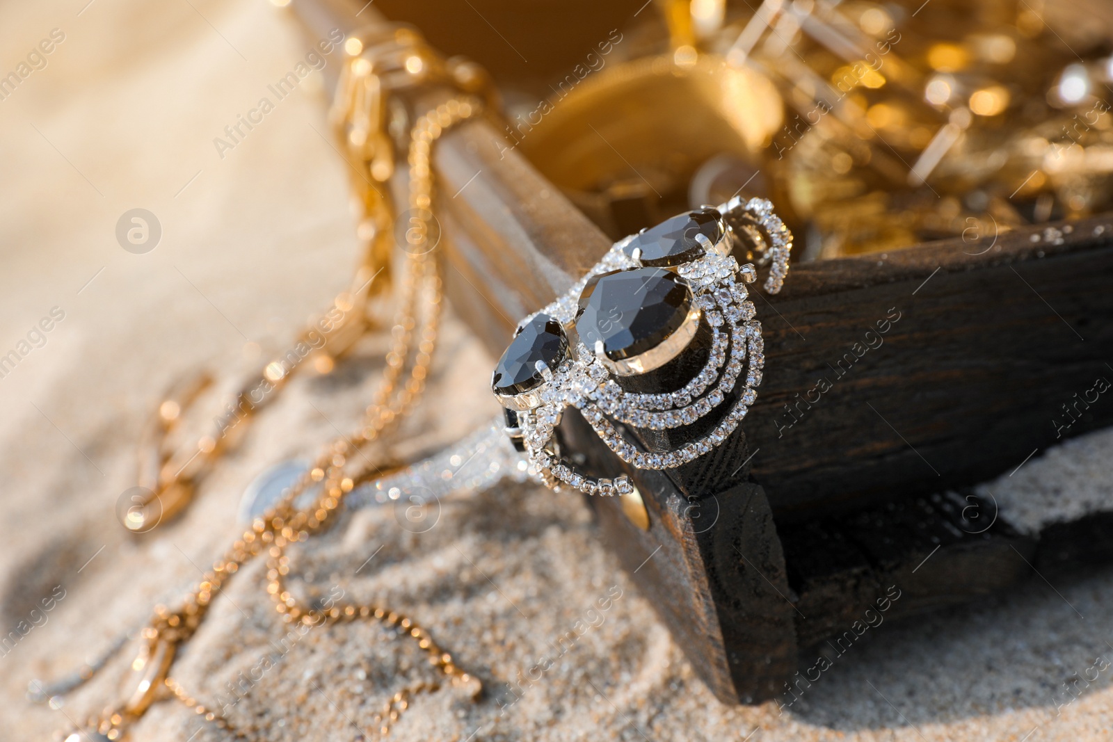 Open wooden chest with treasures on sand, closeup Photo of Open wooden chest with treasures on sand, closeup