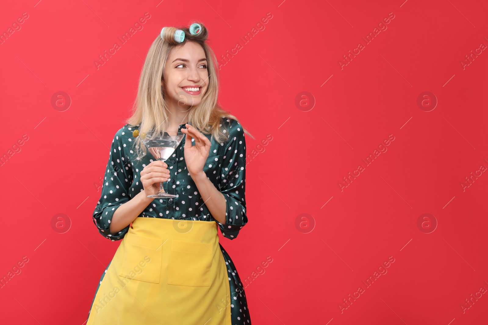 Young housewife with glass of martini on red background. Space for text Photo of Young housewife with glass of martini on red background. Space for text