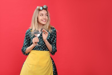 Young housewife with glass of martini on red background. Space for text Photo of Young housewife with glass of martini on red background. Space for text
