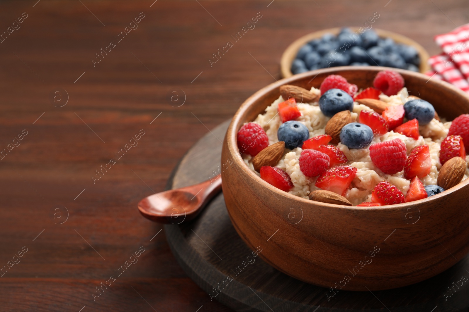 Tasty oatmeal porridge with berries and almond nuts in bowl served on wooden table, space for text Photo of Tasty oatmeal porridge with berries and almond nuts in bowl served on wooden table, space for text