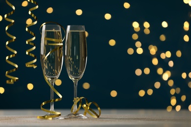 Glasses of champagne and serpentine streamers on table against dark blue background with blurred lights. Space for text Photo of Glasses of champagne and serpentine streamers on table against dark blue background with blurred lights. Space for text