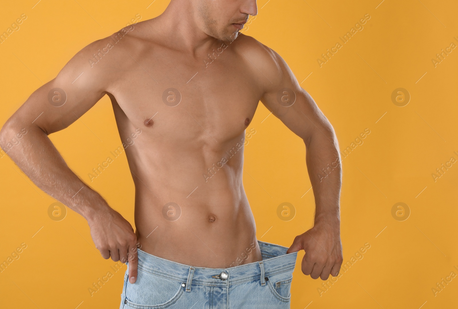 Shirtless man with slim body wearing big jeans on yellow background, closeup Photo of Shirtless man with slim body wearing big jeans on yellow background, closeup
