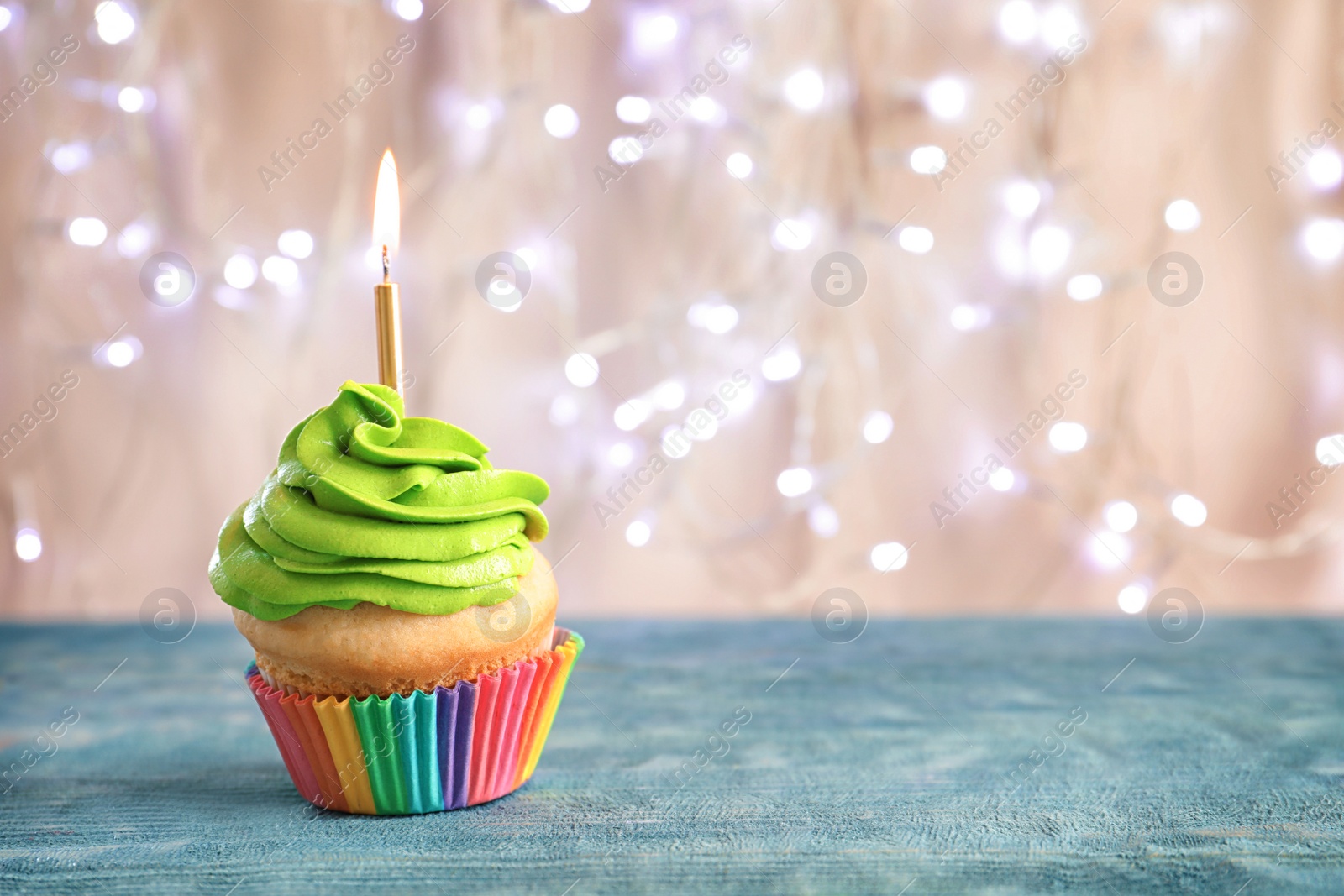 Birthday cupcake with burning candle on table against blurred lights Photo of Birthday cupcake with burning candle on table against blurred lights