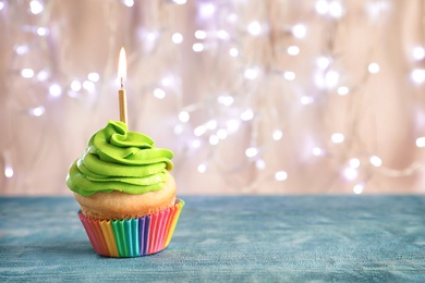 Birthday cupcake with burning candle on table against blurred lights Photo of Birthday cupcake with burning candle on table against blurred lights