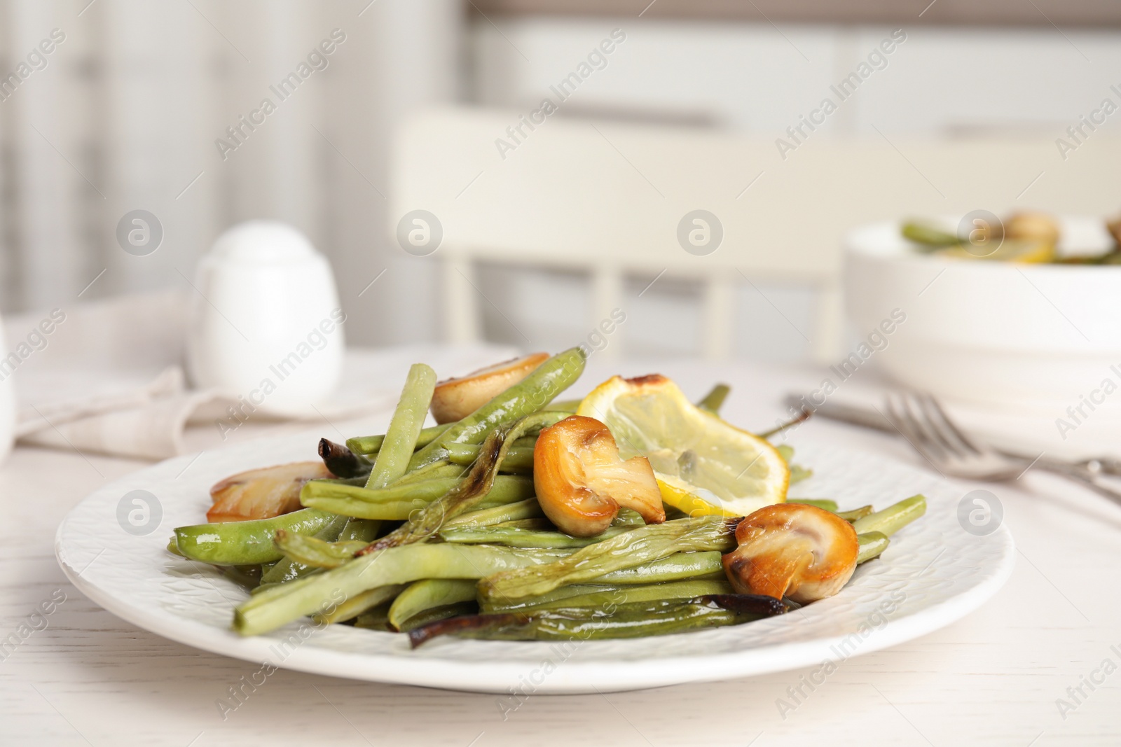 Delicious baked green beans with lemon and mushrooms on white table, closeup Photo of Delicious baked green beans with lemon and mushrooms on white table, closeup