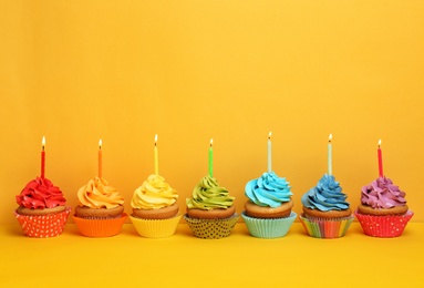 Birthday cupcakes with candles on color background Photo of Birthday cupcakes with candles on color background