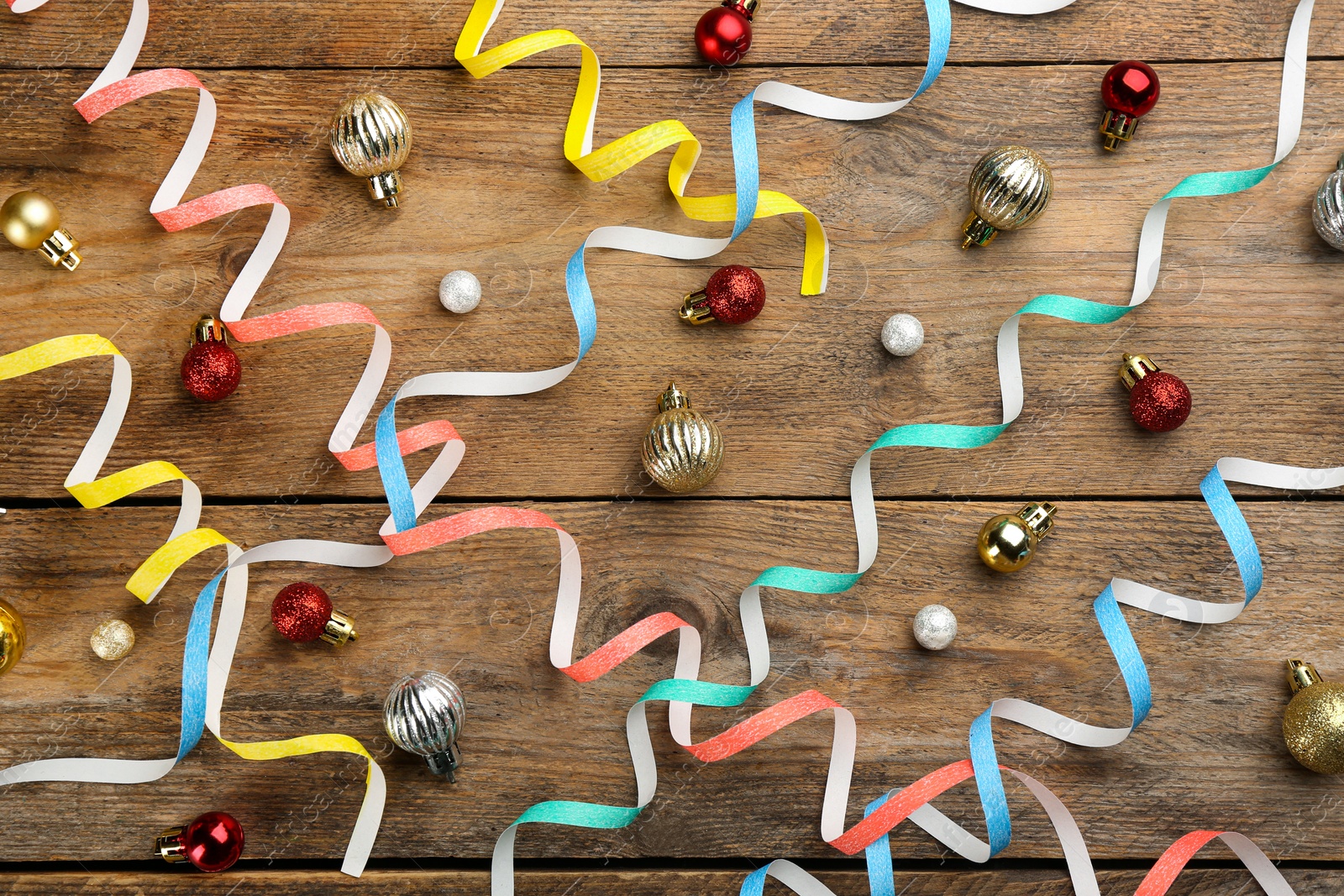 Colorful serpentine streamers and Christmas balls on wooden background, flat lay Photo of Colorful serpentine streamers and Christmas balls on wooden background, flat lay