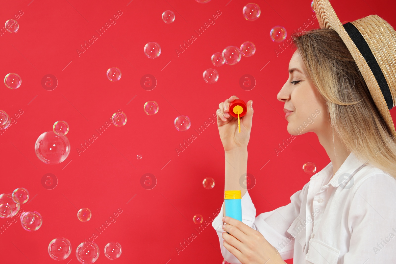 Young woman blowing soap bubbles on red background, space for text Photo of Young woman blowing soap bubbles on red background, space for text