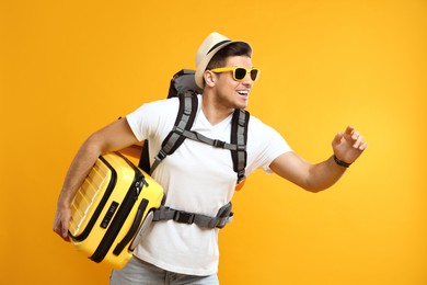 Male tourist with travel backpack and suitcase on yellow background Photo of Male tourist with travel backpack and suitcase on yellow background