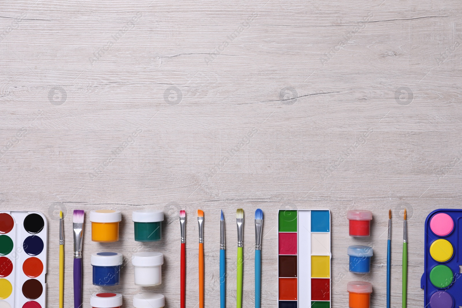 Photo of Different paints and brushes on wooden table, flat lay. Space for text