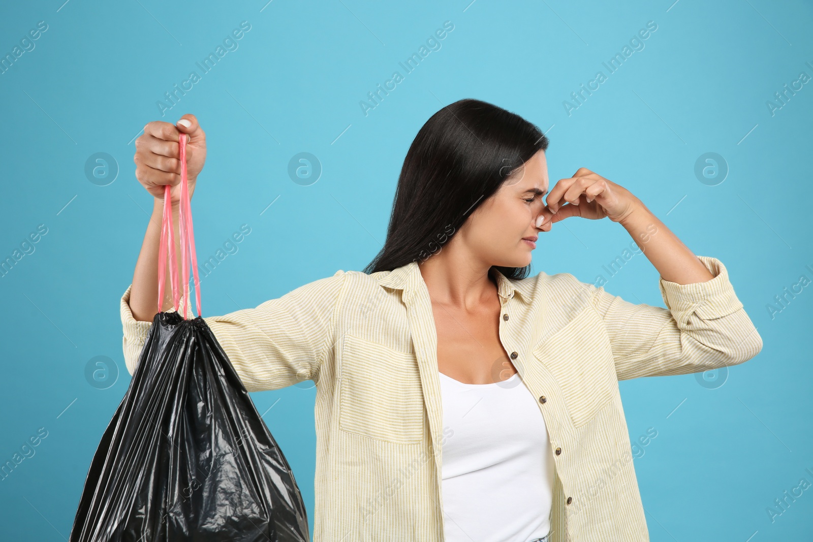 Woman holding full garbage bag on light blue background Photo of Woman holding full garbage bag on light blue background