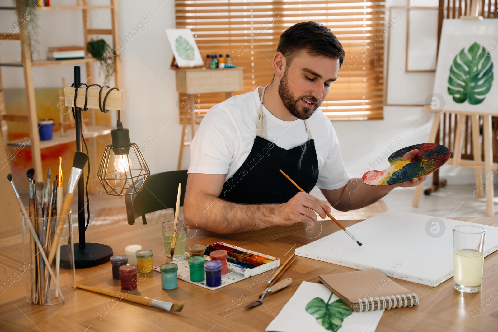 Young man painting with brush in artist studio Photo of Young man painting with brush in artist studio
