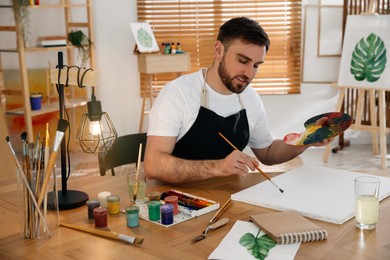 Young man painting with brush in artist studio Photo of Young man painting with brush in artist studio