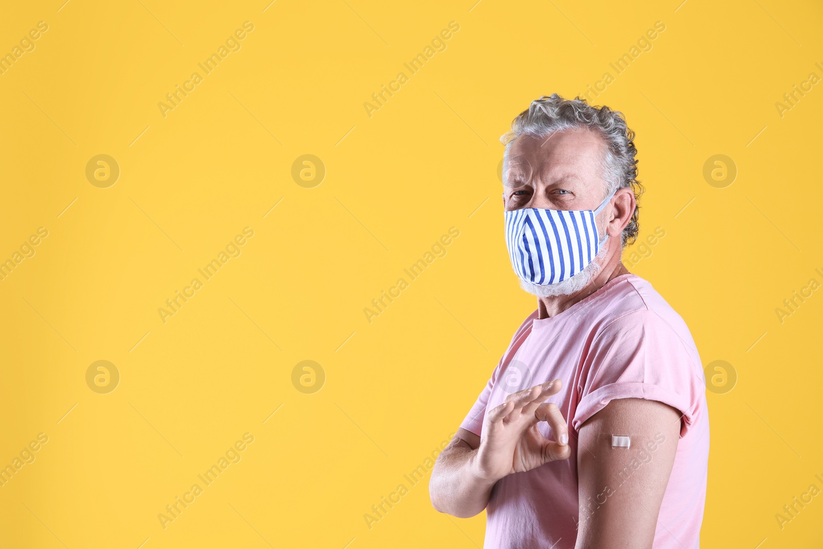 Cheerful senior man showing arm with bandage after vaccination on yellow background. Space for text Photo of Cheerful senior man showing arm with bandage after vaccination on yellow background. Space for text