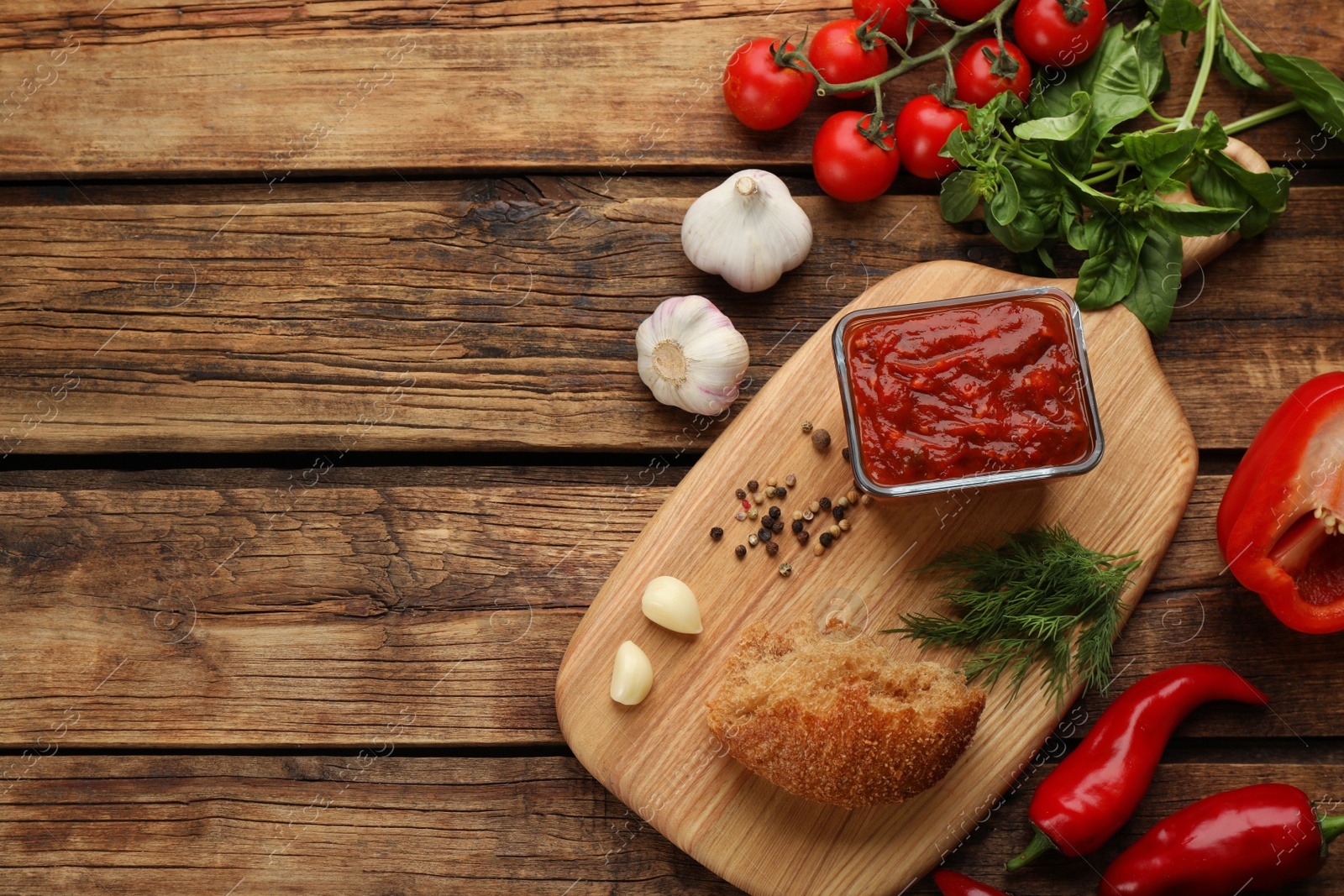 Delicious adjika sauce in bowl with bread and ingredients on wooden table, flat lay. Space for text Photo of Delicious adjika sauce in bowl with bread and ingredients on wooden table, flat lay. Space for text