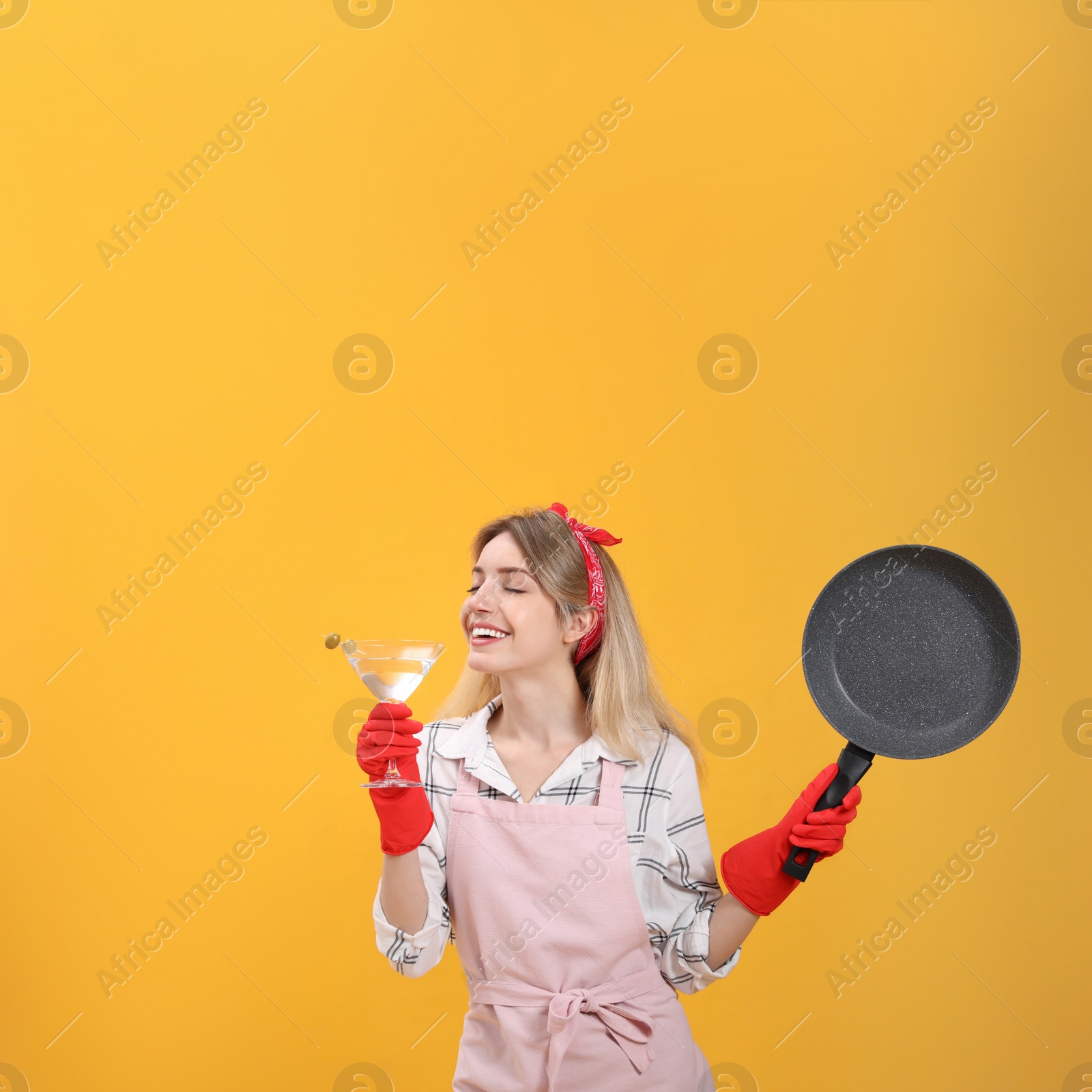 Young housewife with frying pan and glass of martini on yellow background Photo of Young housewife with frying pan and glass of martini on yellow background