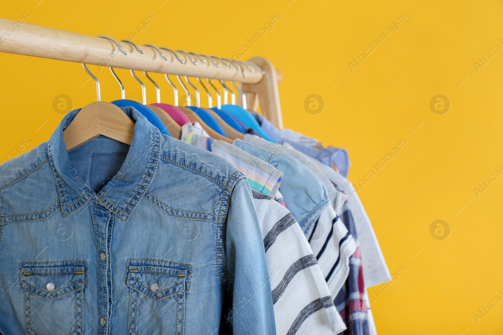 Rack with stylish children clothes on yellow background, closeup. Space for text Photo of Rack with stylish children clothes on yellow background, closeup. Space for text