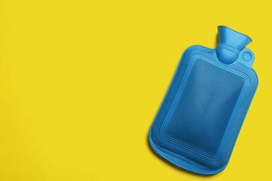 Photo of Blue rubber hot water bottle on yellow background, top view. Space for text