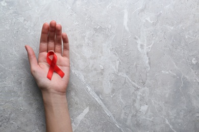 Woman holding red awareness ribbon at light grey marble table, top view with space for text. World AIDS disease day Photo of Woman holding red awareness ribbon at light grey marble table, top view with space for text. World AIDS disease day