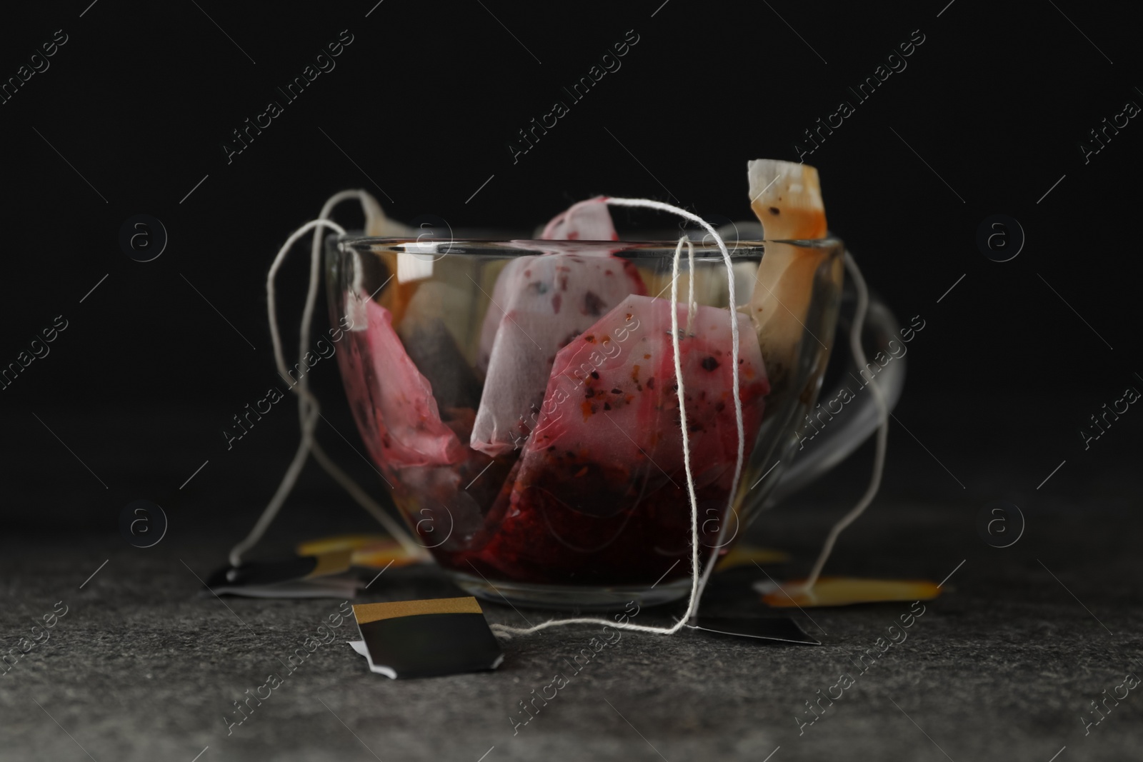 Many used tea bags in glass cup on grey table Photo of Many used tea bags in glass cup on grey table