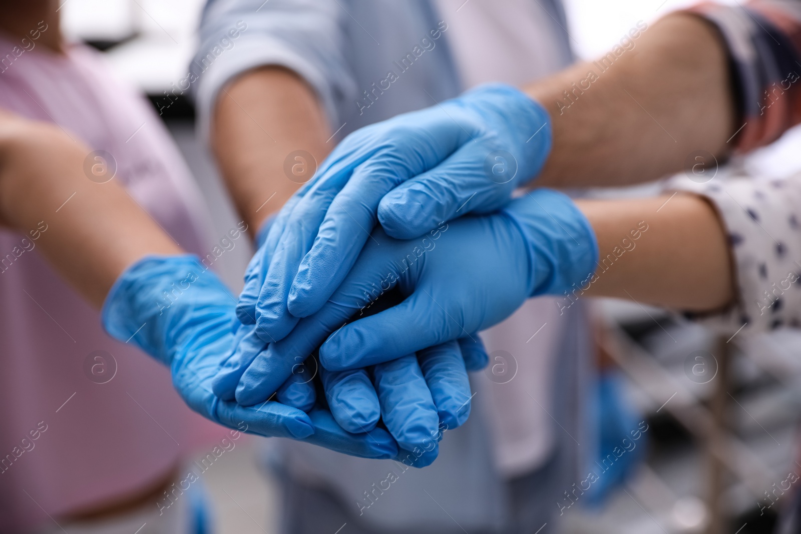 Photo of Group of people in blue medical gloves stacking hands indoors, closeup