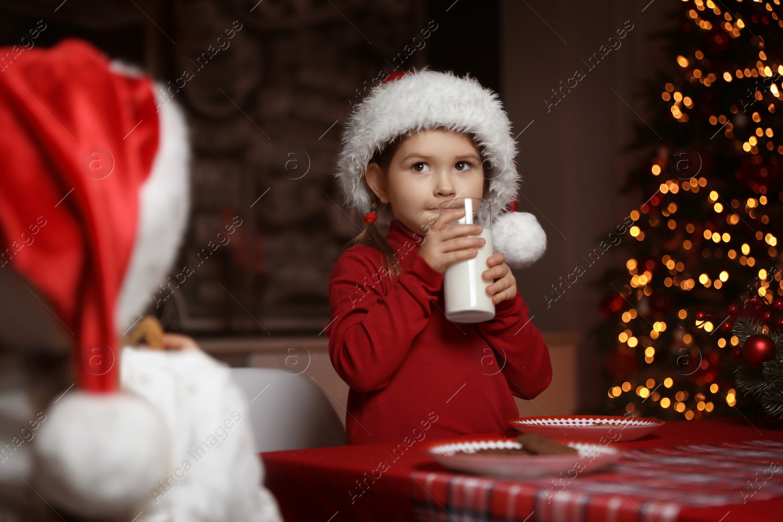 Cute little child with glass of milk at table in dining room. Christmas time Photo of Cute little child with glass of milk at table in dining room. Christmas time