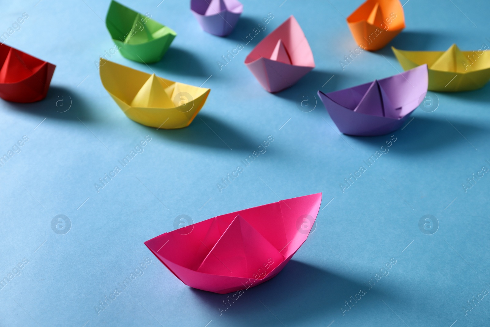 Bright pink paper boat standing out from colorful ones on light blue background. Diversity concept Photo of Bright pink paper boat standing out from colorful ones on light blue background. Diversity concept